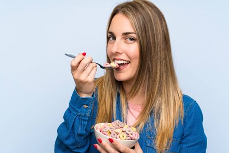 Young woman with bowl of cereals over isolated blue wall