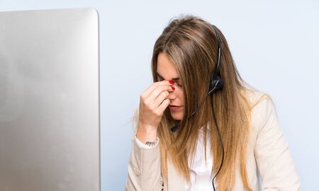 Young blonde telemarketer woman over isolated blue wall and stressedの写真素材