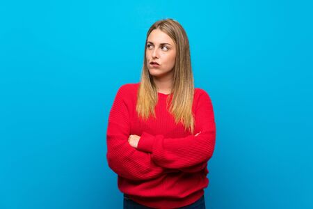 Woman with red sweater over blue wall with confuse face expressionの写真素材