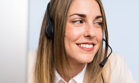 Young blonde telemarketer woman over isolated blue wall and smiling