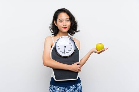 Young asian girl with weighing machine over isolated white backgroundの写真素材