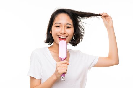 Asian young woman over isolated background with hair combの写真素材