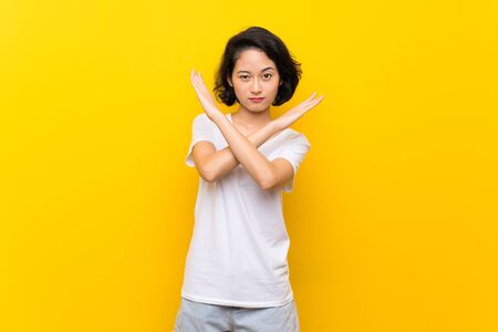 Asian young woman over isolated yellow wall making NO gestureの写真素材