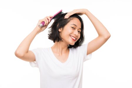Asian young woman over isolated background with hair combの写真素材
