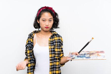 Young artist woman holding a palette over isolated white background with sad expressionの写真素材