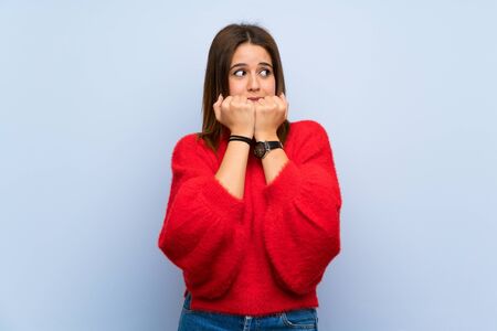 Young woman over isolated blue wall nervous and scared putting hands to mouthの写真素材