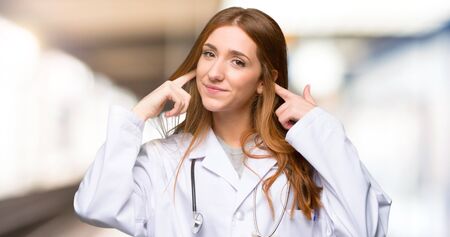 Redhead doctor woman covering both ears with hands in the hospitalの写真素材