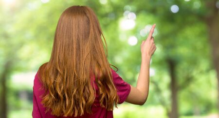 Young redhead girl pointing back with the index finger in the parkの写真素材