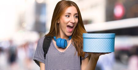 Redhead student woman holding gift box in hands in the city
