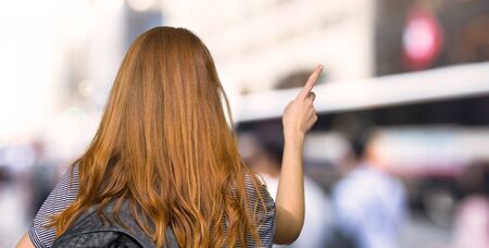 Redhead student woman pointing back with the index finger in the cityの写真素材