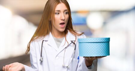 Redhead doctor woman holding gift box in hands in the hospitalの写真素材