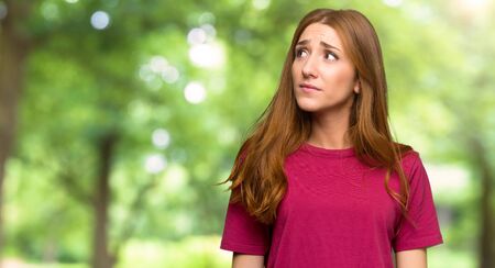Young redhead girl looking up with serious face in the parkの写真素材