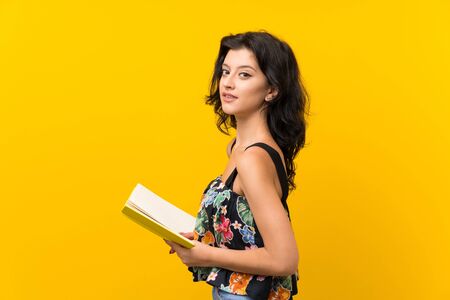 Young woman over isolated yellow background holding and reading a bookの写真素材