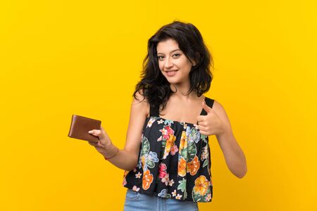 Young woman over isolated yellow background holding a wallet