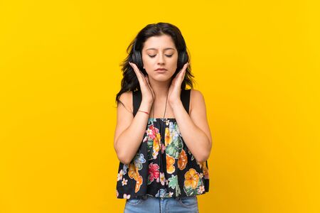 Young woman over isolated yellow background listening to music with headphonesの写真素材