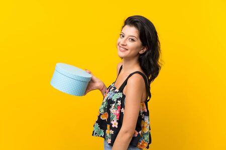 Young woman over isolated yellow background holding gift box