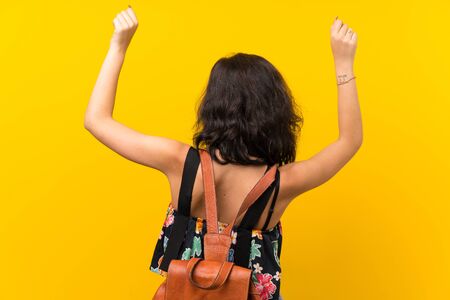 Young woman over isolated yellow background with backpackの写真素材