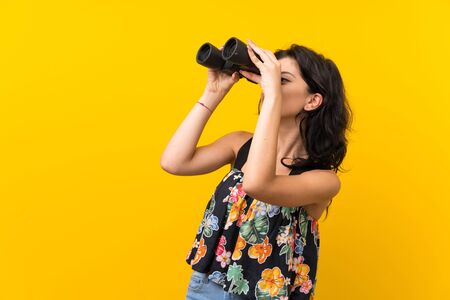 Young woman over isolated yellow background with black binocularsの写真素材