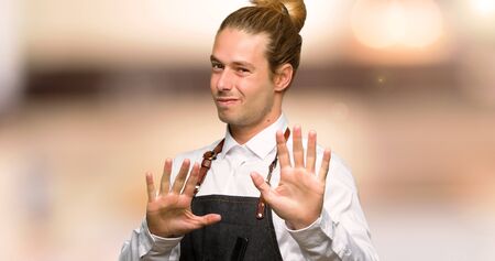 Barber man in an apron is a little bit nervous and scared stretching hands to the front in a barber...