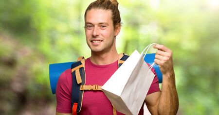 Hiker man with mountain backpacker holding a lot of shopping bags in the mountain