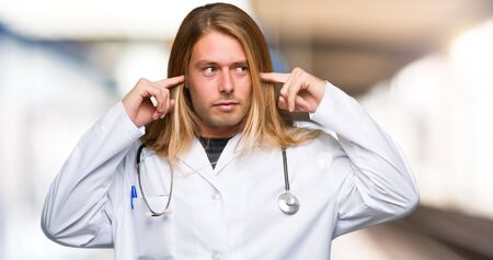 Doctor man covering both ears with hands in a hospitalの写真素材