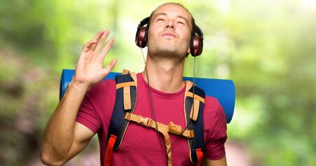 Hiker man with mountain backpacker listening to music with headphones and dancing in the mountain