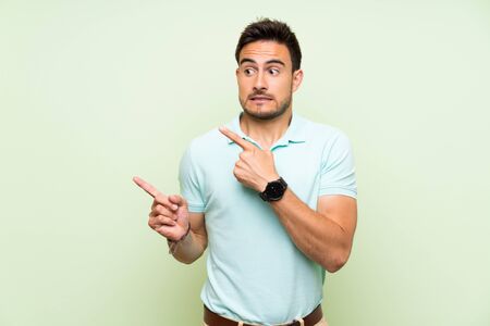 Handsome young man over isolated background frightened and pointing to the sideの写真素材