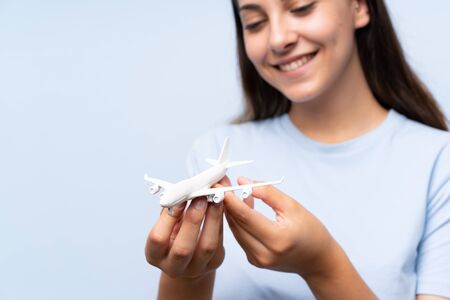 Young woman over isolated blue wall holding a toy airplane