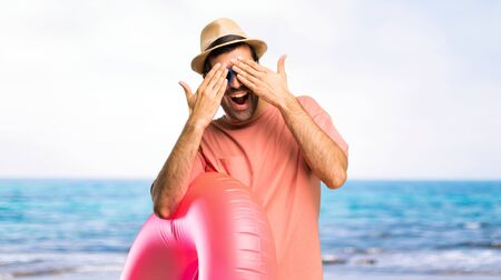 Man with hat and sunglasses on his summer vacation covering eyes by hands. Surprised to see what is ahead at the beachの写真素材