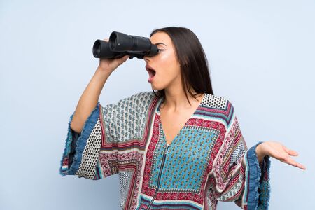 Young woman over isolated blue wall with black binocularsの写真素材