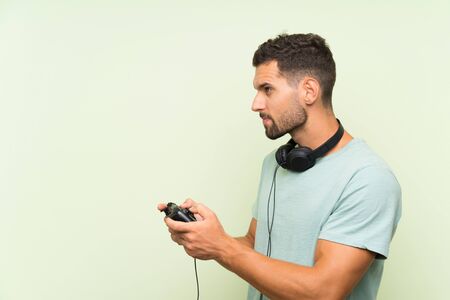 Young handsome man playing with a video game controller over isolated green wallの写真素材
