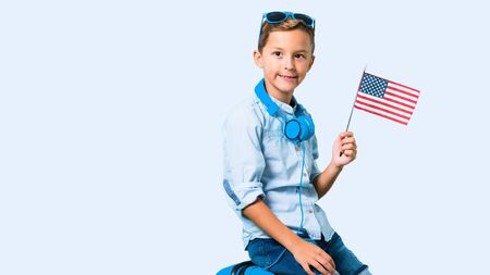 Boy with sunglasses and headphones traveling with his suitcase holding an american flag on blue backgroundの写真素材