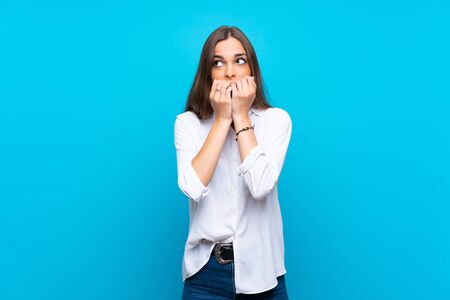 Young woman over isolated blue background nervous and scared putting hands to mouthの写真素材
