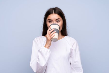 Young woman over isolated blue background holding and drinking a coffee to take awayの写真素材