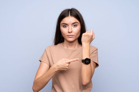 Young woman over isolated blue background showing the hand watch with serious expressionの写真素材