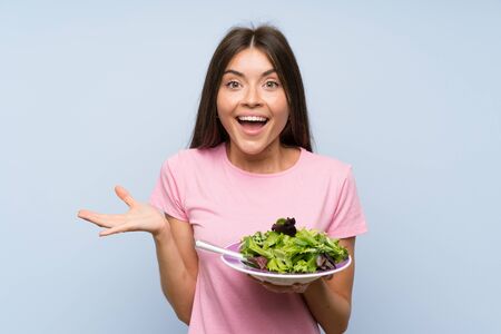 Young woman with salad over isolated blue background with shocked facial expressionの写真素材