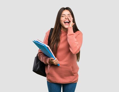 Young student woman holding notebooks shouting and announcing something over isolated grey backgroundの写真素材