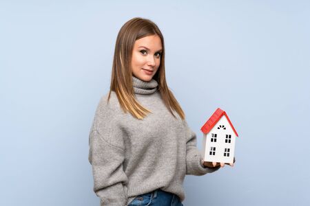 Teenager girl with sweater over isolated blue background holding a little houseの写真素材