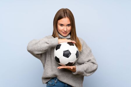 Teenager girl with sweater over isolated blue background holding a soccer ballの写真素材