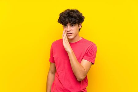 Young man over isolated yellow wall whispering somethingの写真素材