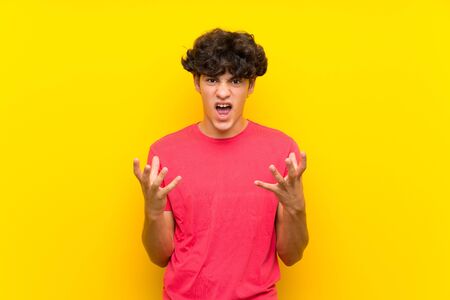 Young man over isolated yellow wall unhappy and frustrated with somethingの写真素材