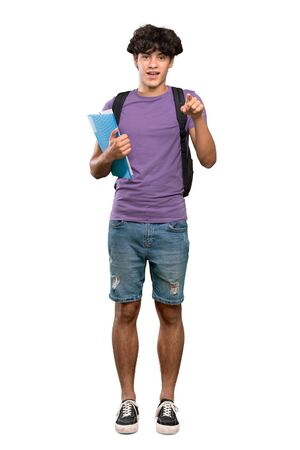A full-length shot of a Young student man surprised and pointing front over isolated white backgroundの写真素材