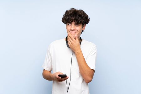 Young man listening music with a mobile over isolated blue wall thinking an ideaの写真素材