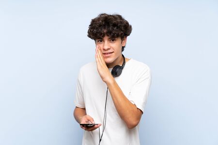 Young man listening music with a mobile over isolated blue wall whispering somethingの写真素材