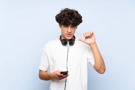 Young man listening music with a mobile over isolated blue wall proud and self-satisfiedの写真素材