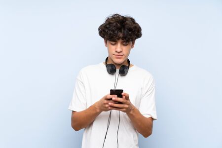 Young man listening music with a mobile over isolated blue wallの写真素材