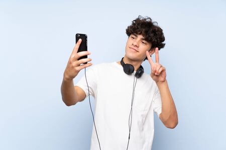 Young man listening music with a mobile over isolated blue wallの写真素材