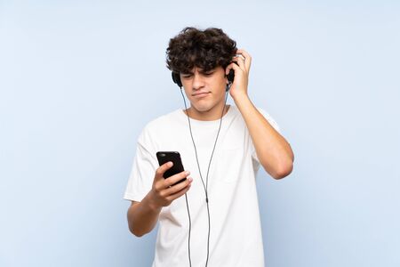 Young man listening music with a mobile over isolated blue wallの写真素材