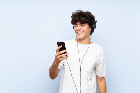 Young man listening music with a mobile over isolated blue wallの写真素材