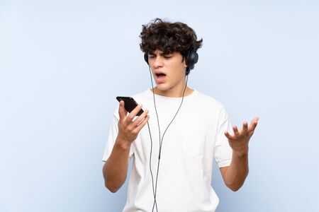 Young man listening music with a mobile over isolated blue wallの写真素材